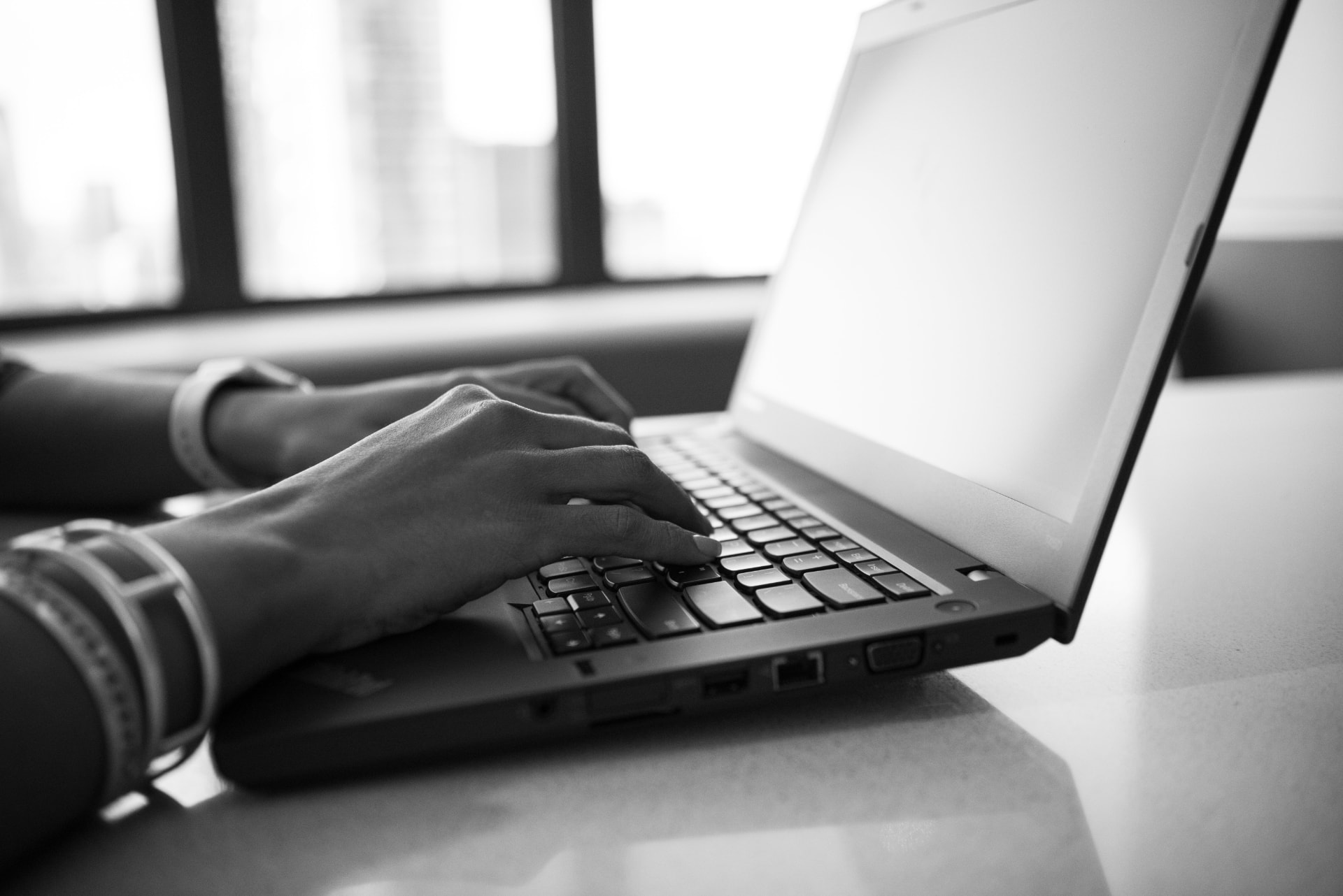 Hands typing on a laptop by a bright window